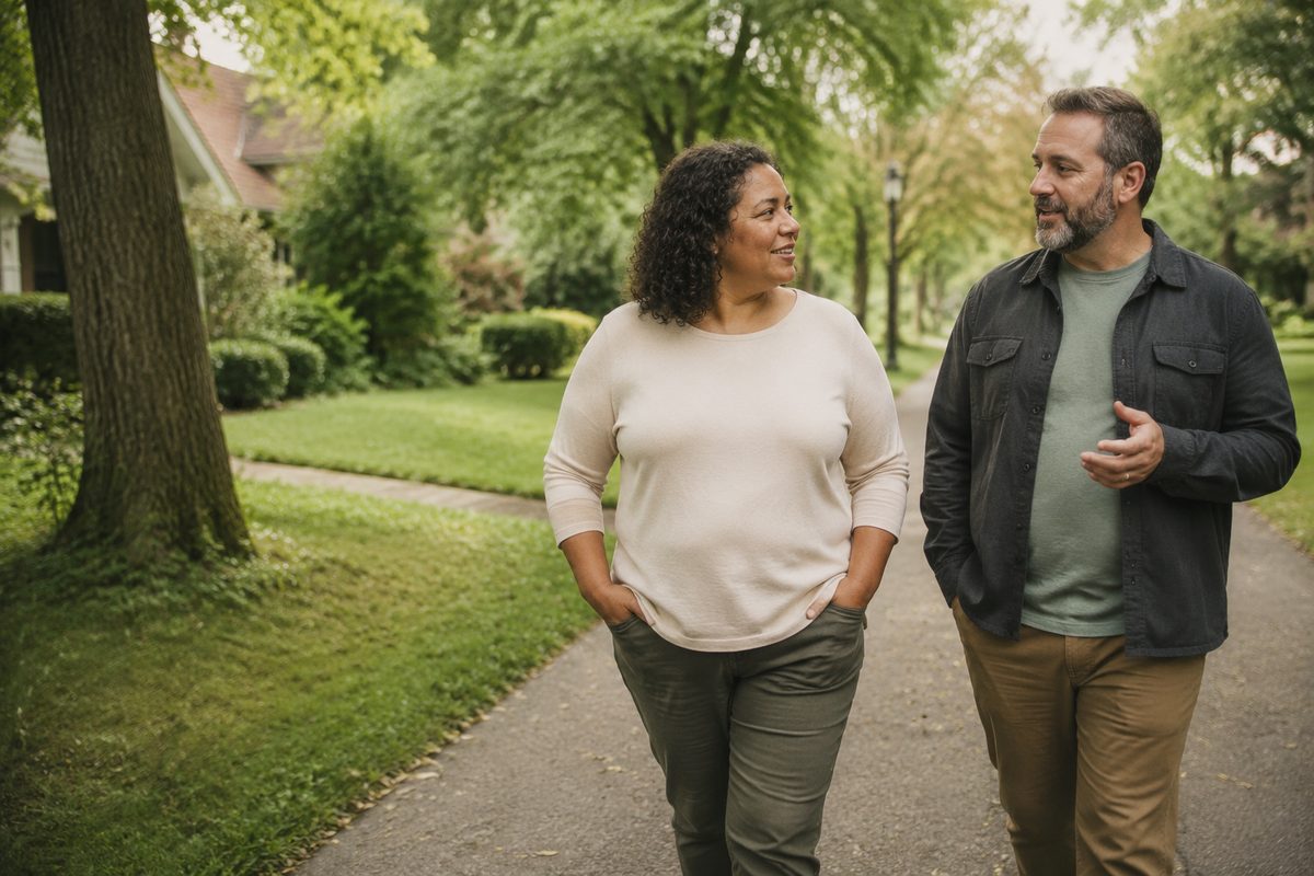 Two people walking side by side and talking on a leaf-strewn residential street.